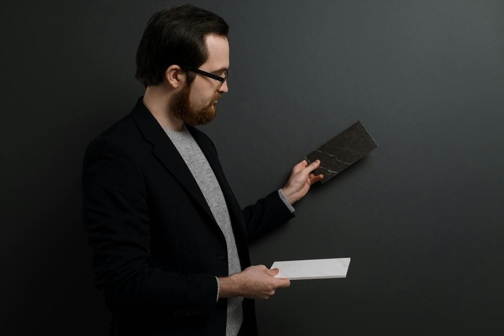 Designer holding two marble samples against a dark wall for material comparison