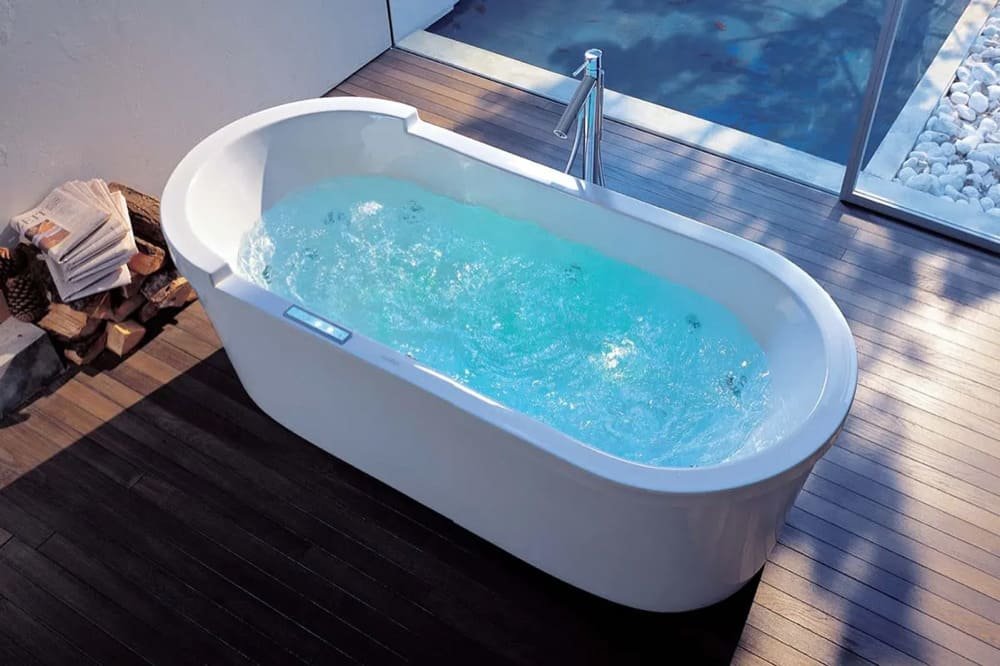Jacuzzi bathtub with bubbling water on wooden deck near towels and white stones