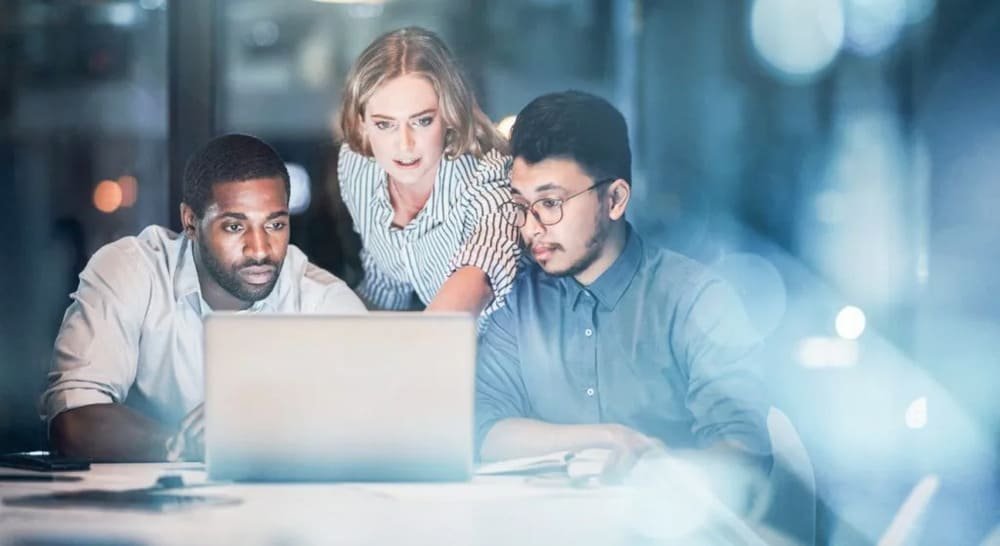 Three people collaboratively looking at a laptop screen in an office setting