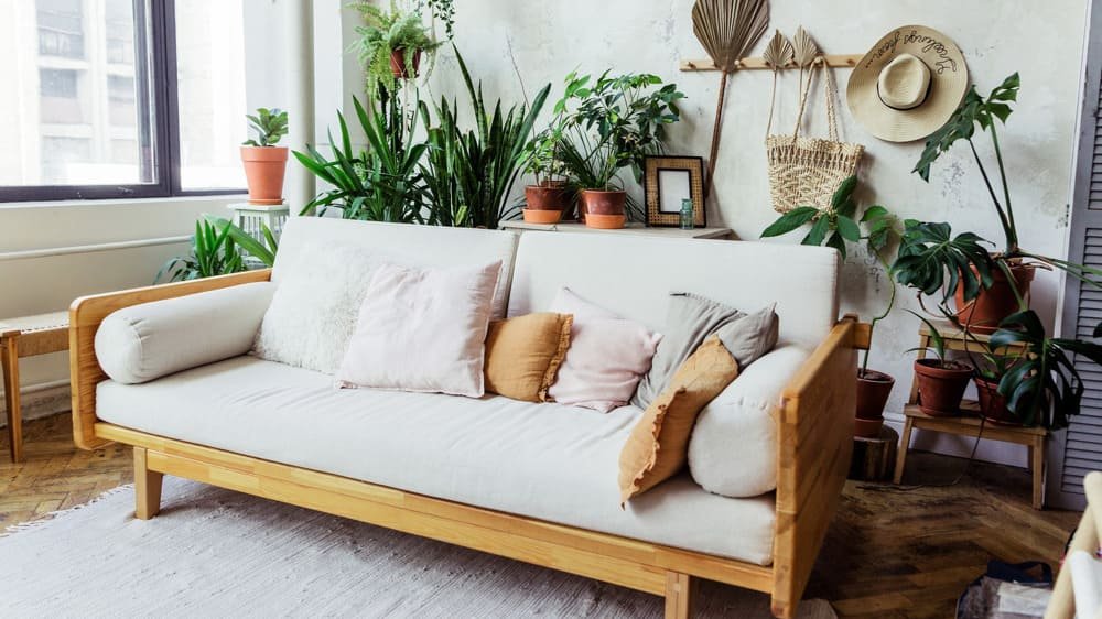 A living room with a wooden frame sofa, colorful throw pillows, and numerous potted plants