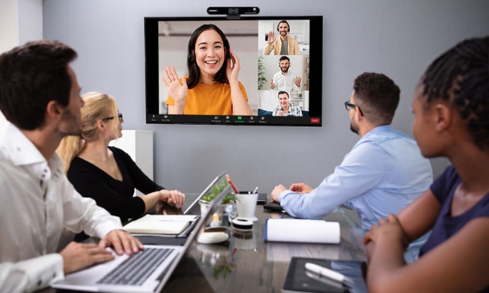 People in a conference room engaged in a video call with participants displayed on a large screen