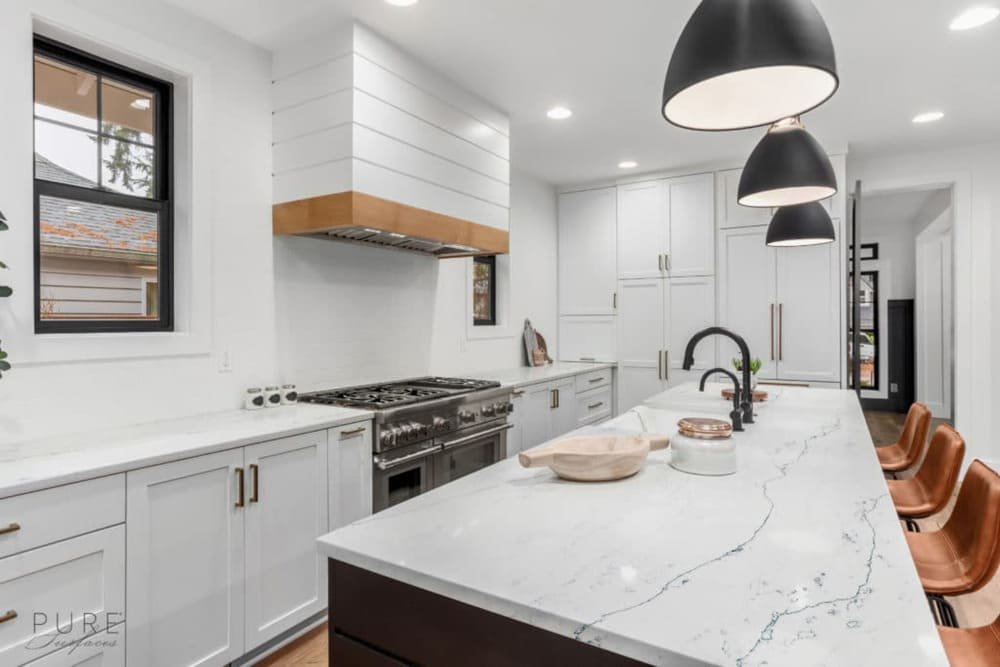 Modern minimalist white kitchen with quartz island, black pendant lights, and brown leather bar stools