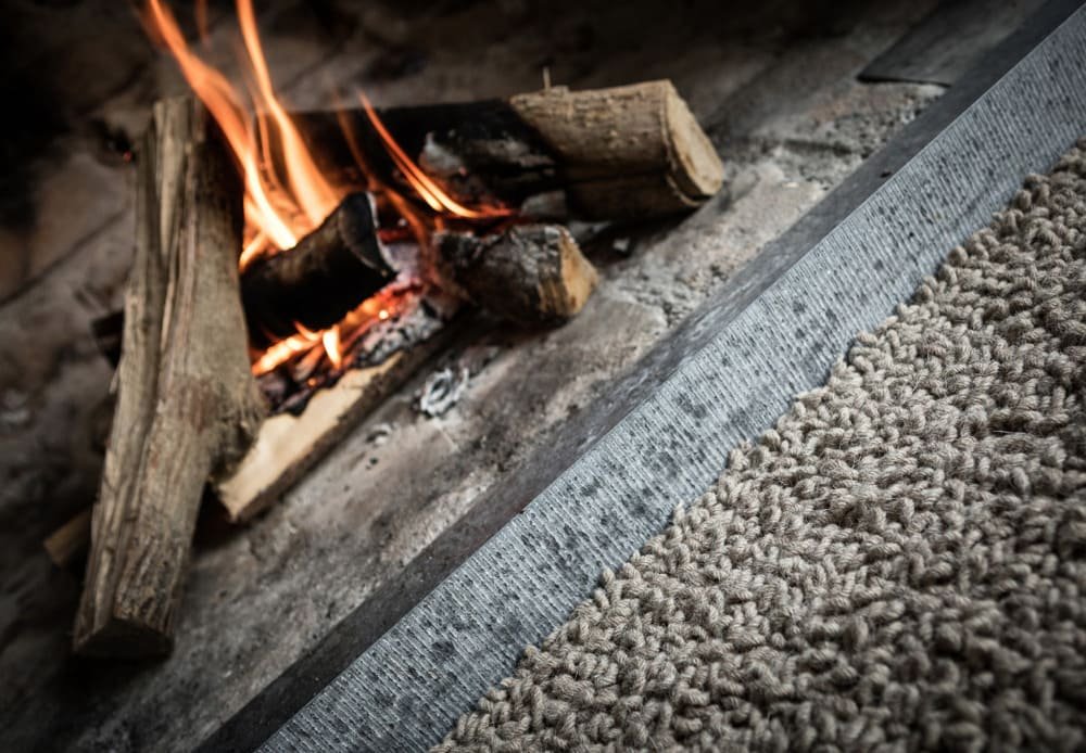 Close-up of a burning fireplace with logs and a wool carpet in the foreground