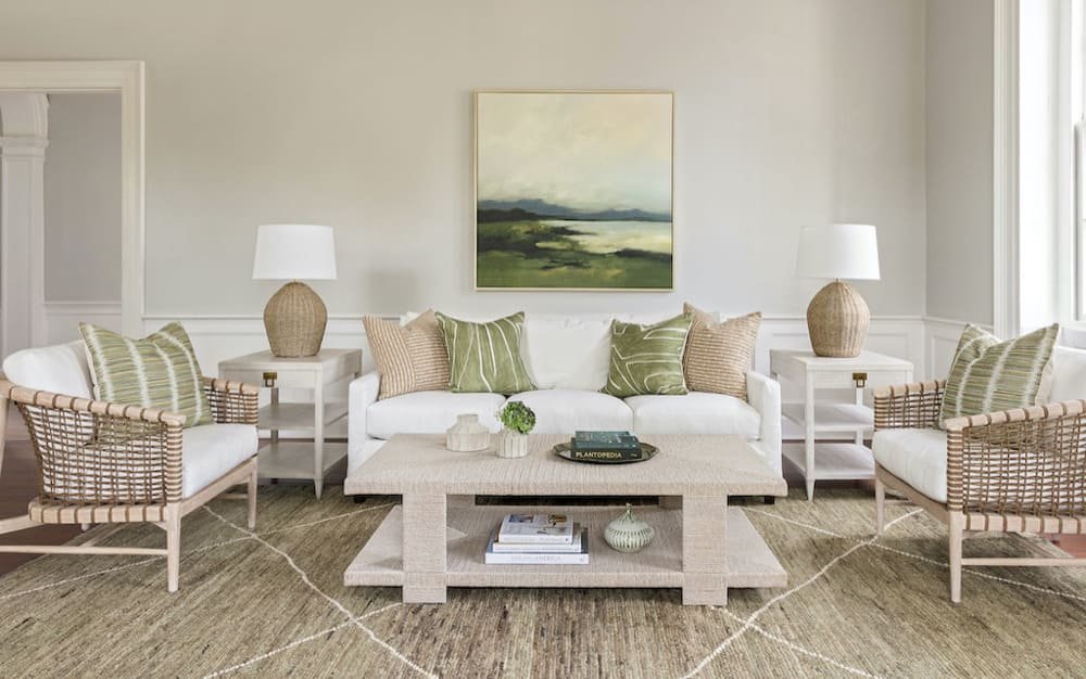 A stylish living room with a white sofa, wicker armchairs, green and beige pillows, a wooden coffee table, and soft lighting