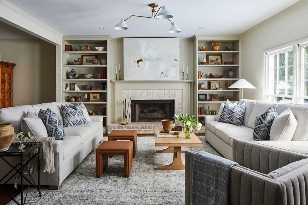Living room with light gray sofas, a brick fireplace, built-in shelves, and natural light from a large window