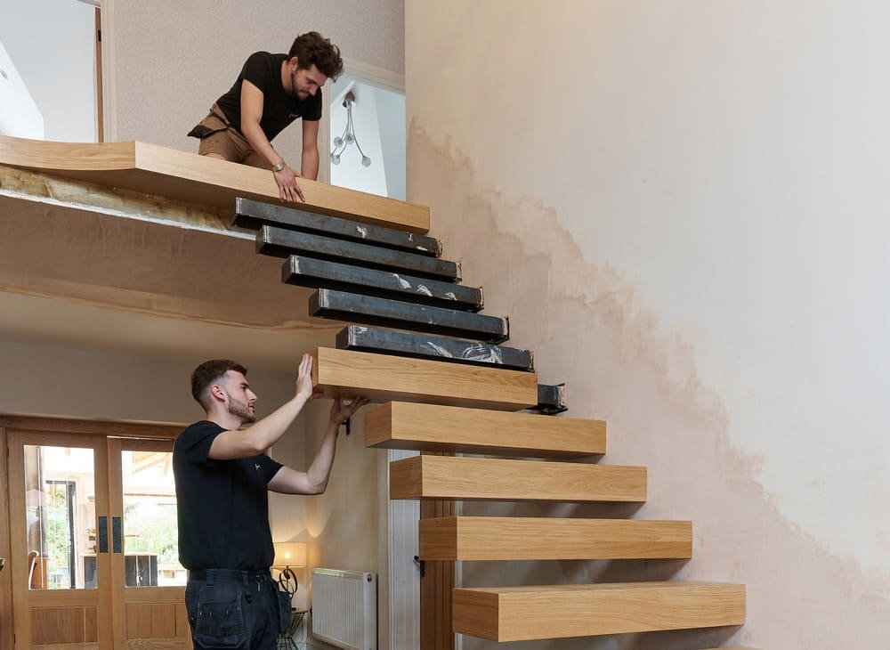 Two men assembling a floating wooden staircase in a home interior