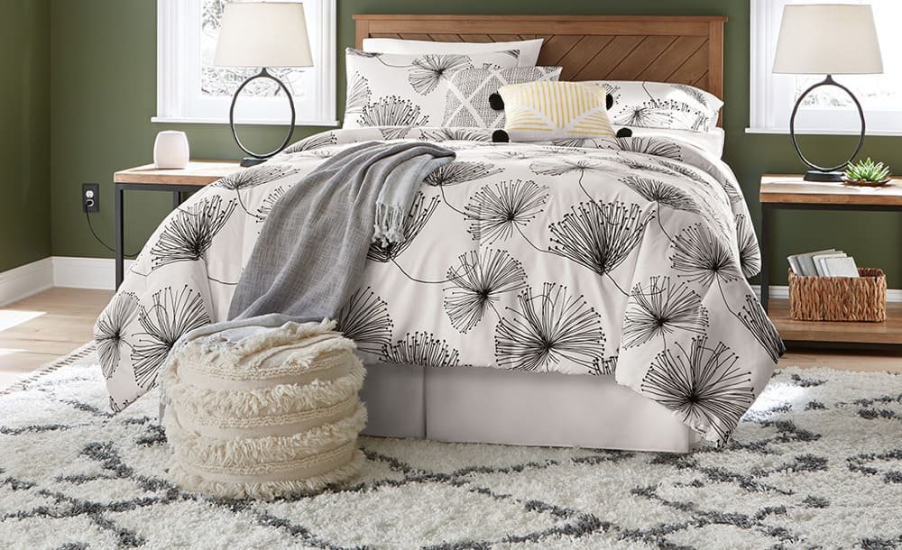 A bedroom with a bed featuring a botanical-patterned comforter and a wooden headboard, flanked by nightstands and lamps