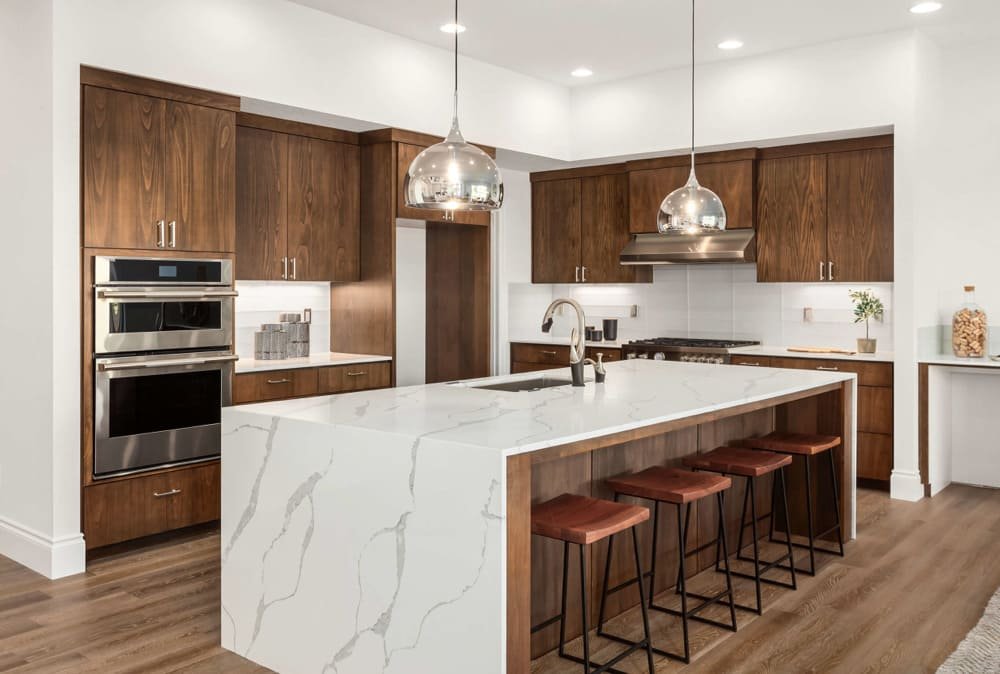 Modern kitchen with wood cabinets, white marble island, pendant lights, and stainless steel appliances